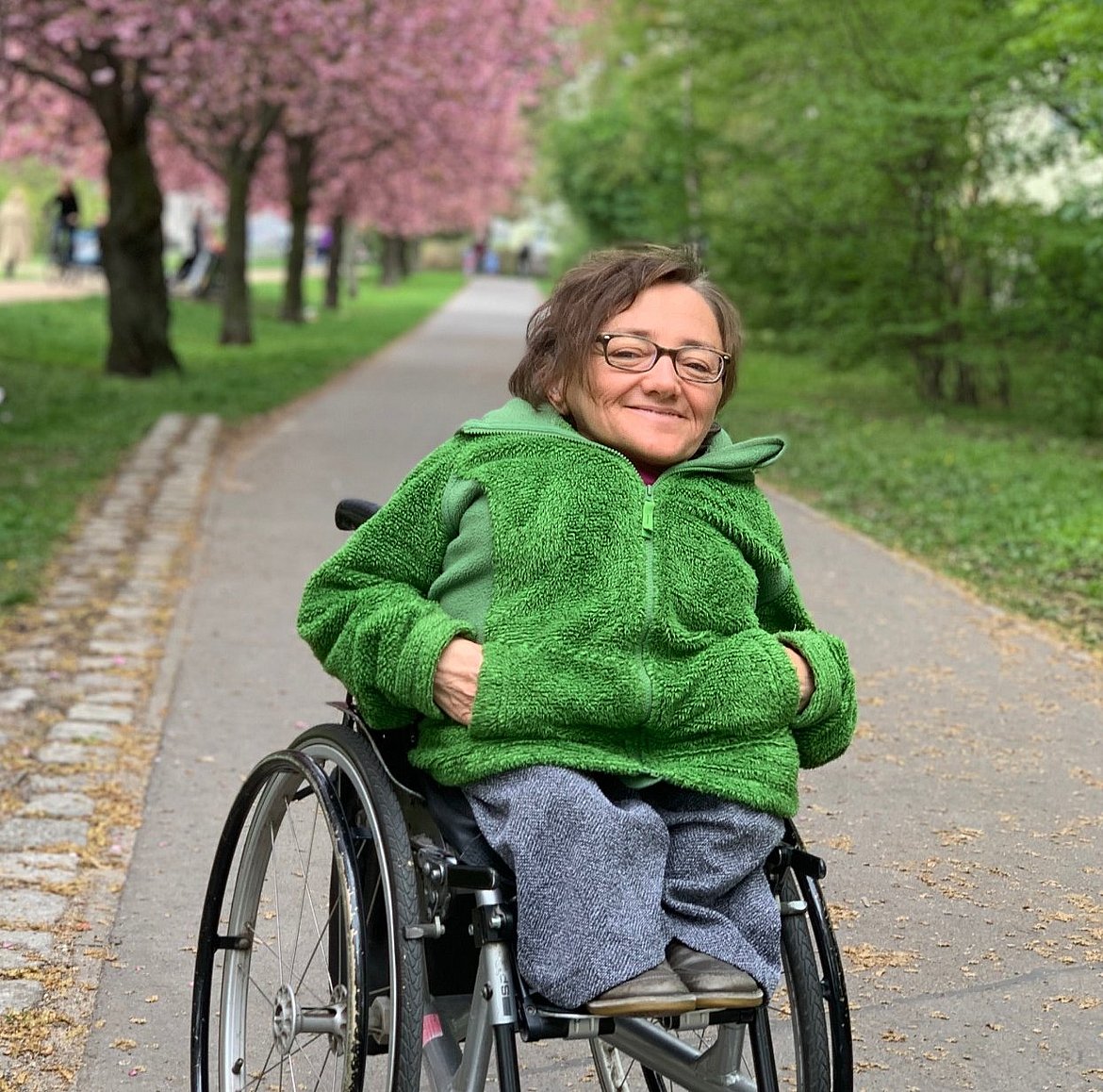 Rebecca Maskos mit Rollstuhl auf einem Weg unter Bäumen