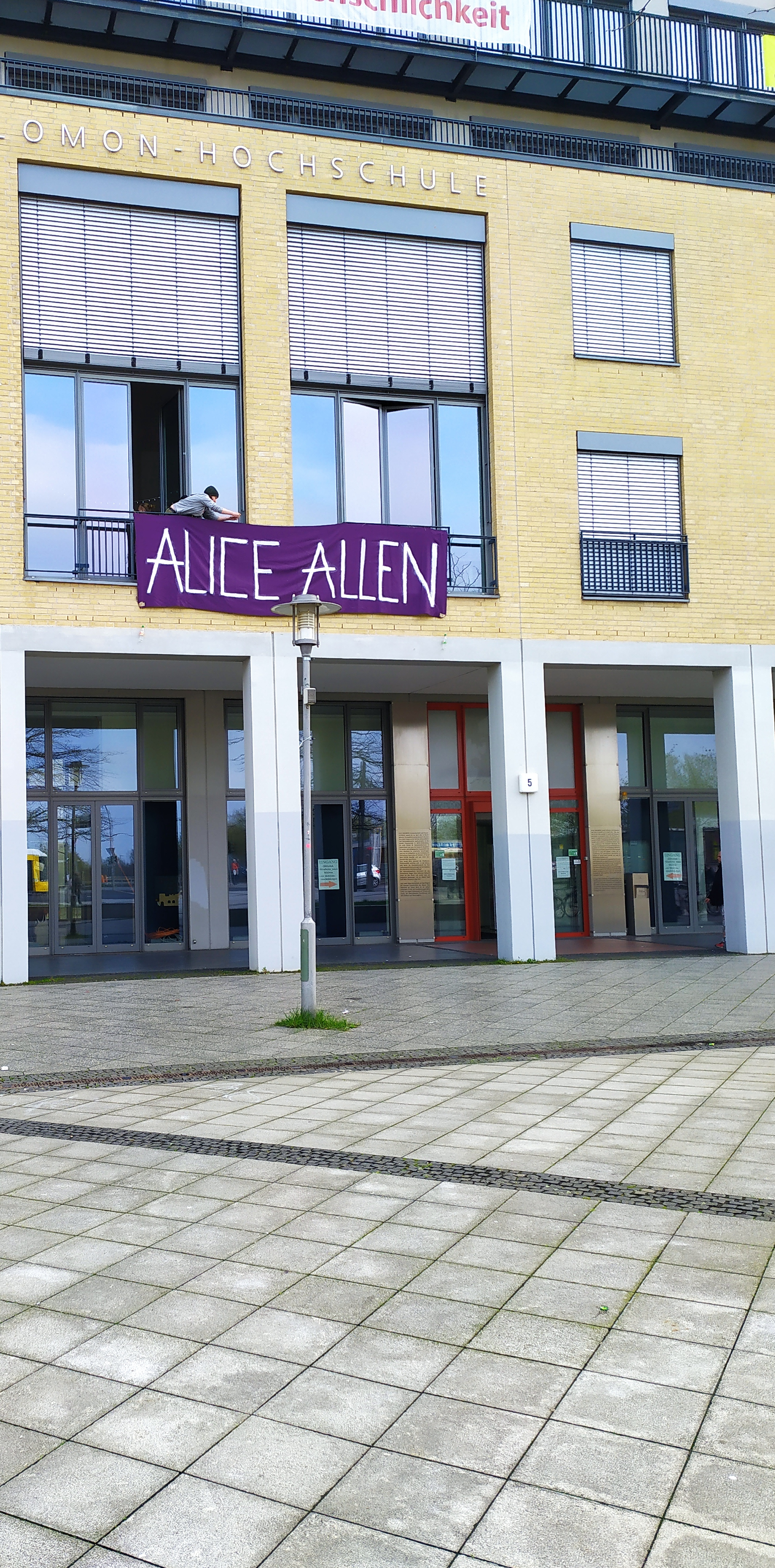 Das Gebäude der Hochschule mit dem Banner in Lila Farbe. Auf dem Banner steht "ALICE ALLEN". 