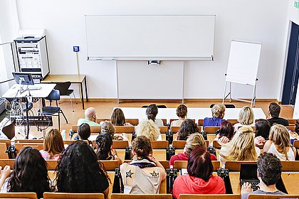 Blick von hinten über einen Hörsaal, Studierende sitzen in den Rängen, vorne eine leere Tafel