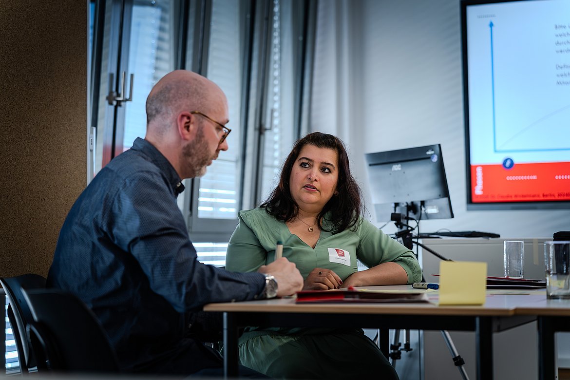 Eine Frau in einer grünen Bluse und ein Mann in einem blauen Hemd diskutieren während eines Workshops.