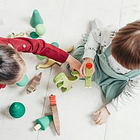 Auf dem Foto sind zwei Kleinkinder beim Spielen mit Holzspielzeug zu sehen.