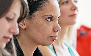 Drei Studentinnen schauen nach vorne, Fokus auf dem Profil der mittleren Studentin.