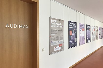 Auf dem Foto sind Plakate vor dem Audimax zu sehen. Die Plakate sind Teil einer Ausstellung gegen Sexismus. 