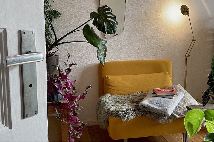 Eine Couch und eine Pflanze in indirektem Licht einer Stehlampe bilden eine Idee eines Sozialen Wohnzimmers.