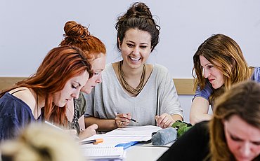 Drei Studentinnen des Master of Arts Studiengangs Biografisches und Kreatives Schreiben sitzen an einem Tisch und machen Notizen.