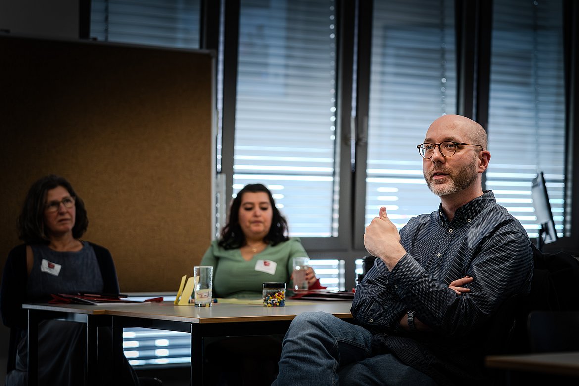 Ein sitzender Mann spricht während eines Workshops. Er gestikuliert mit seinen Händen zur Betonung.