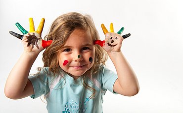 Lachendes Mädchen zeigt Hände mit bunten Fingermalfarben dies nimmt Bezug auf Master of Arts Studiengang Dialogische Qualitätsentwicklung in den Frühen Hilfen und im Kinderschutz