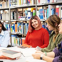 Studierende der ASH Berlin sitzen in der Bibliothek an einem Tisch und unterhalten sich
