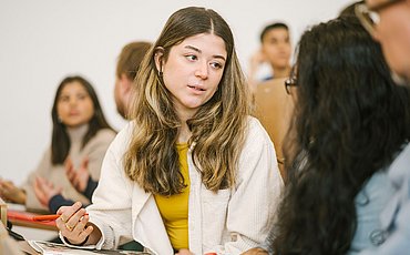 Auf dem Foto sind Studierende der ASH Berlin zu sehen, die nebeneinander in einem Hörsaal sitzen und sich unterhalten.