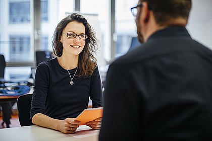 Beratungsgespräch: die Forschungsreferentin sitzt einem Wissenschaftler an einem Tisch gegenüber und berät ihn.