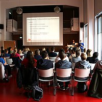 Foto vom Audimax in dem ungefähr 70 Personen sitzen und einem Vortrag zuhören