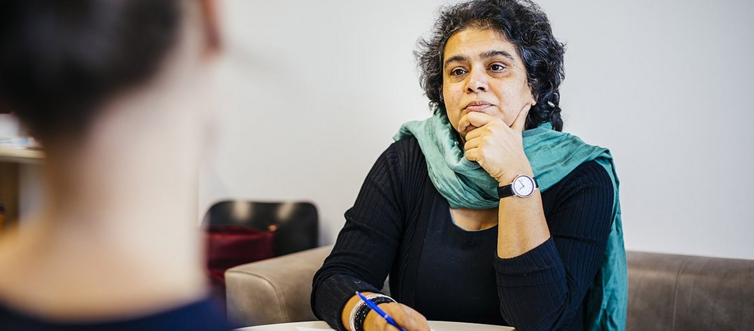 Interview-Situation: Eine Probantin ist nur von hinten sichtbar und scheint zu erzählen, eine Professorin hört aufmerksam zu.