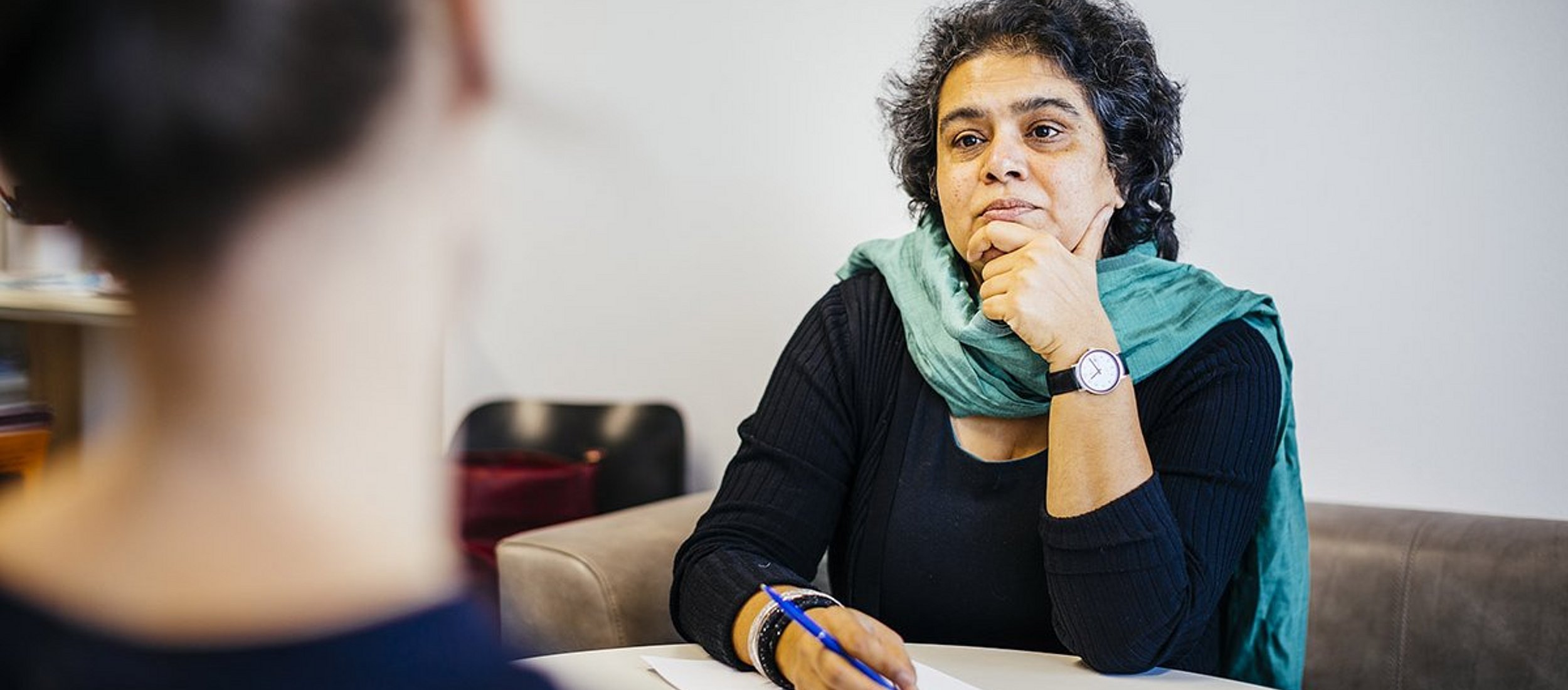 Interview-Situation: Eine Probantin ist nur von hinten sichtbar und scheint zu erzählen, eine Professorin hört aufmerksam zu.